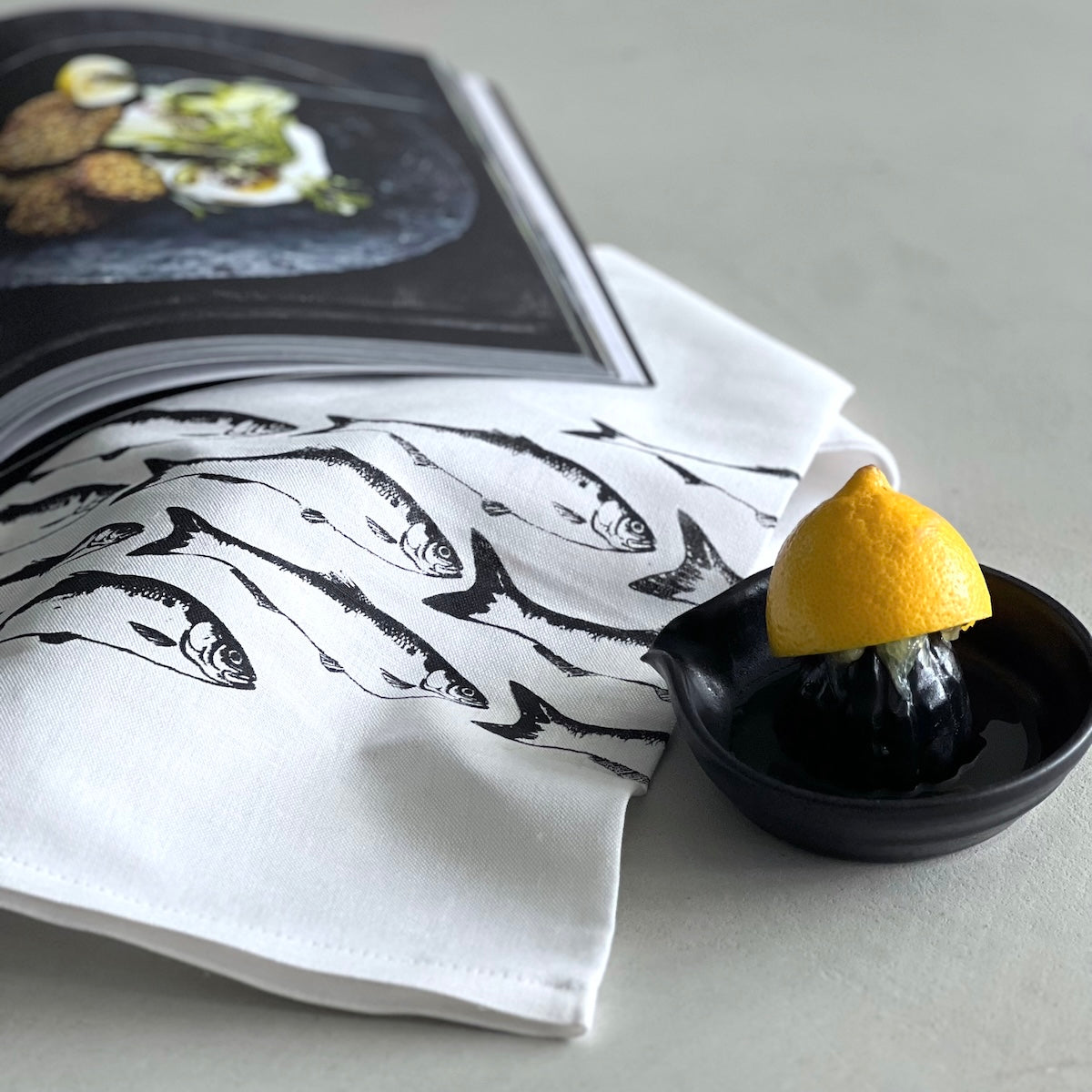 Weißes Geschirrtuch mit Fischen. Zitruspresse aus schwarzer Keramik.